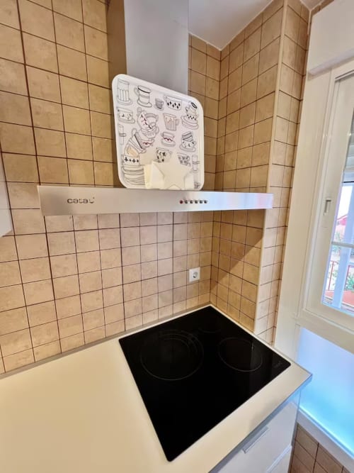 Cocina moderna con placa de inducción negra, campana extractora blanca y paredes de azulejos beige en apartamento de playa en Fuengirola