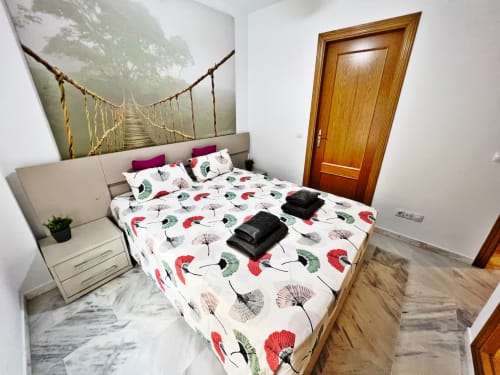 Acogedor dormitorio con ropa de cama floral y vista a la ciudad en apartamento frente al mar de Grupo Inmo House en Fuengirola
