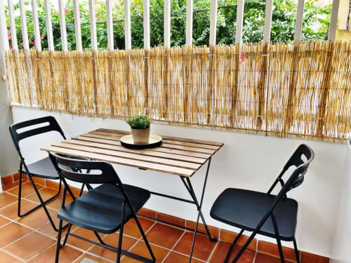 Comedor de apartamento frente al mar en Fuengirola con mesa de madera, sillas negras y biombo de caña con vistas al verde