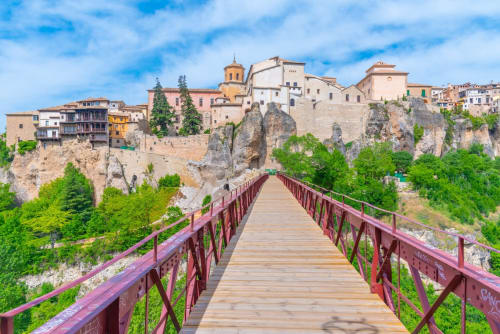 Puente de madera que conduce al pueblo histórico de Cuenca, España, con arquitectura medieval y edificios suspendidos en acantilados