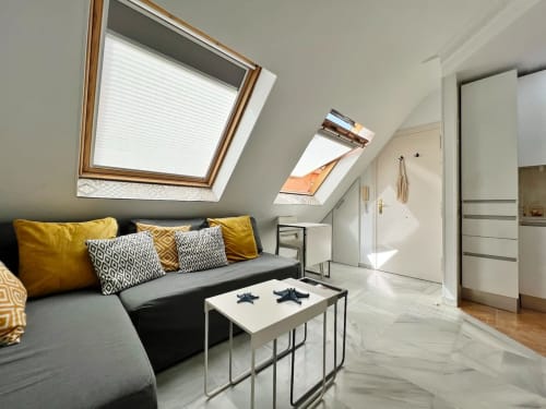 Luminosa habitación abuhardillada en ático-penthouse de Fuengirola con tragaluces, sofá gris, cojines mostaza y decoración moderna