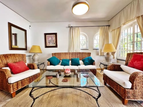 Luminoso salón de apartamento en Fuengirola con muebles de mimbre, cojines turquesa y rojos, mesa de cristal