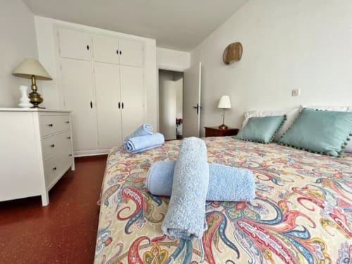Dormitorio de apartamento frente al mar en Fuengirola con ropa de cama estampada colorida, almohadas turquesas, armario blanco y enrollado