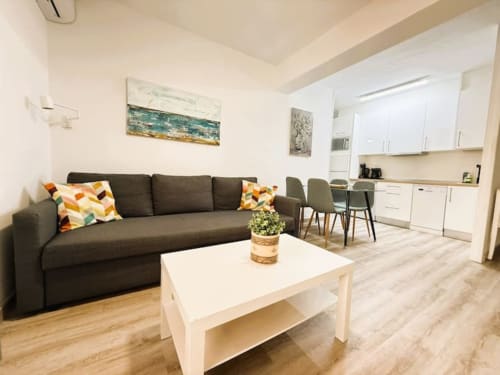 Moderna sala de estar en Fuengirola con sofá gris, mesita de café blanca y cocina abierta