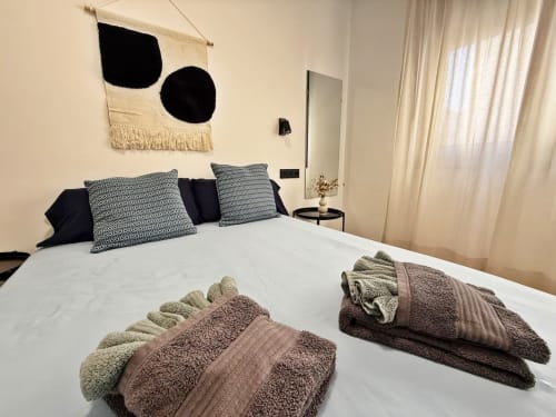 Dormitorio moderno en apartamento de playa en Fuengirola con cama blanca, almohadas estampadas y toallas dobladas