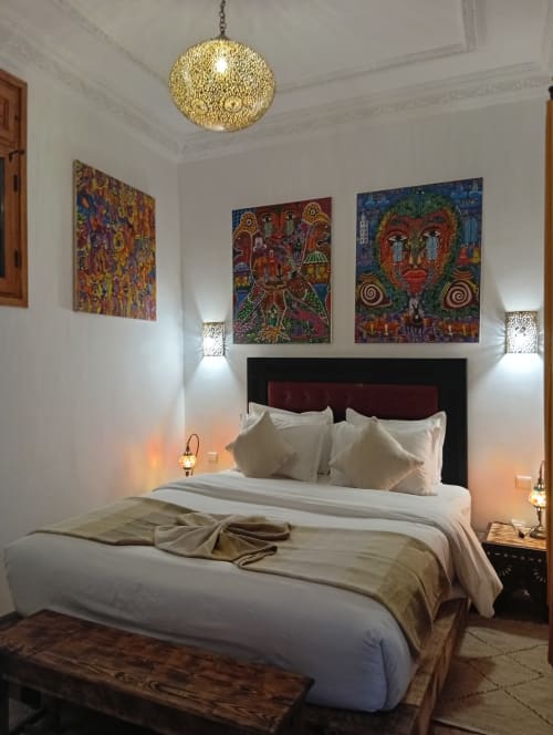 Chambre luxueuse du Riad Le Village Mogador avec art marocain coloré, luminaire doré, literie blanche et décor traditionnel
