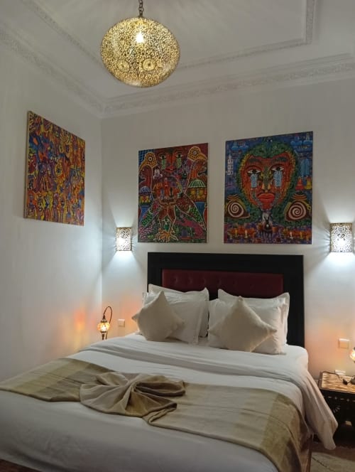 Chambre de luxe au Riad Le Village Mogador à Essaouira avec art marocain coloré, lampe suspendue dorée et literie blanche