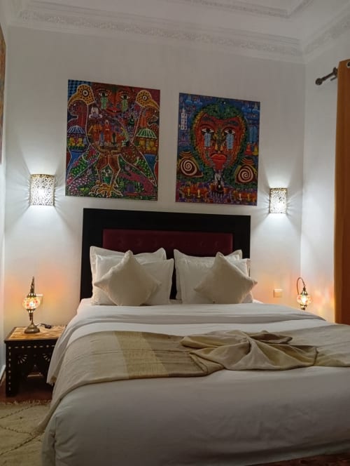 Chambre luxueuse au Riad Le Village Mogador d'Essaouira avec œuvres d'art marocaines colorées, literie blanche et éclairage ambiant