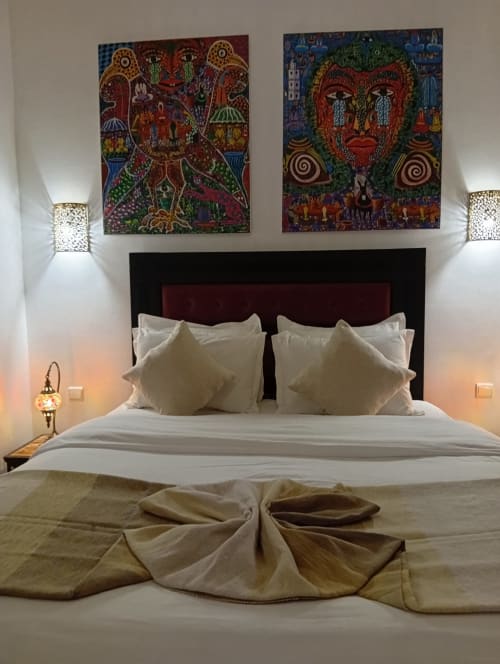 Chambre style marocain au Riad Le Village Mogador avec art tribal coloré, tête de lit bordeaux et literie blanche