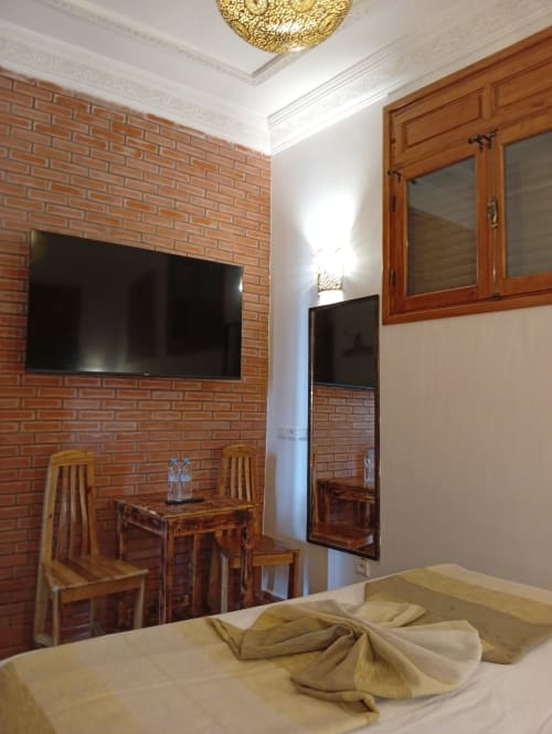 Chambre 1 lit à Riad Le Village Mogador, Essaouira avec murs en brique, lit, TV, mobilier bois et vue sur cour intérieure