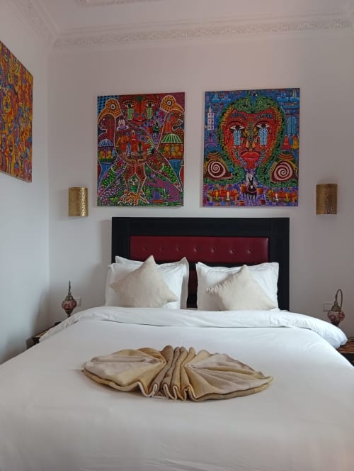 Décoration marocaine colorée au-dessus d'un lit à tête de lit bordeaux et linge blanc au Riad Le Village Mogador, Essaouira