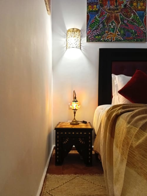 Coin cosy de la chambre au Riad Le Village Mogador avec lampe traditionnelle en laiton, table noire ornementée et éclairage chaleureux