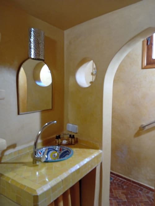 Salle de bain contemporaine avec vasque en marbre jaune, miroir voûté, robinetterie chromée et savonnière bleue au Riad Le Village