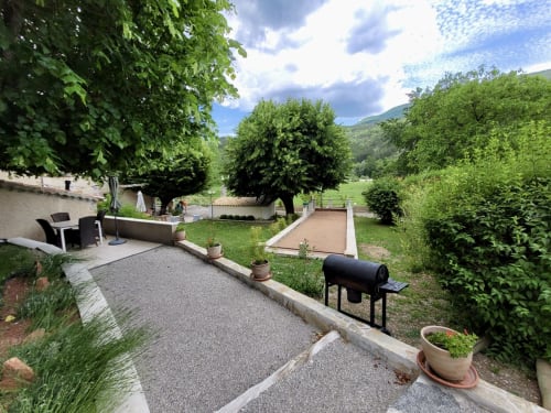 Spacieux jardin arrière du gîte Domaine de la Méouge avec vue montagne, grill, terrain de pétanque et verdure luxuriante