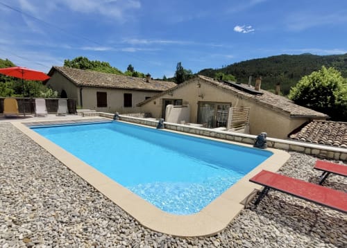 Piscine rectangulaire bleu vif du gîte Domaine de la Méouge à Barret-sur-Méouge, entourée de chaises longues et de pierre