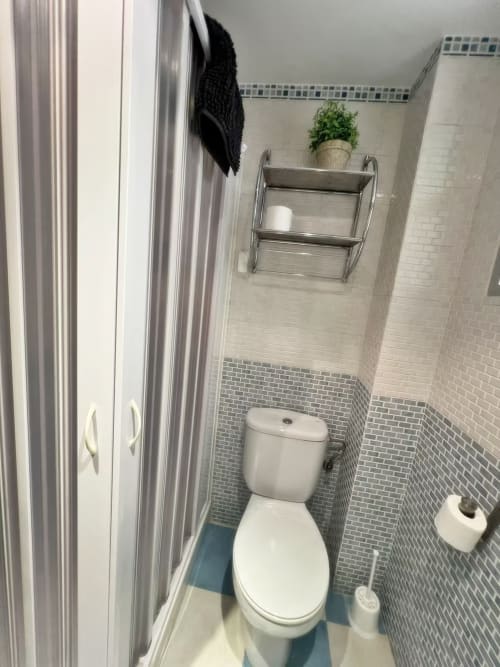 Baño moderno en apartamento de Fuengirola con inodoro blanco, paredes alicatadas, estantería metálica y planta decorativa