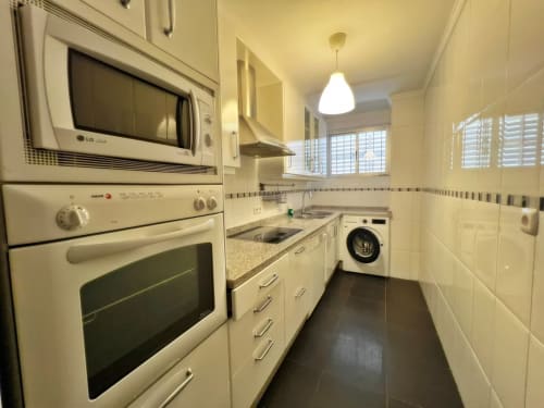 Cocina moderna en apartamento de Fuengirola con muebles color crema, encimeras de granito y suelo de azulejos oscuros
