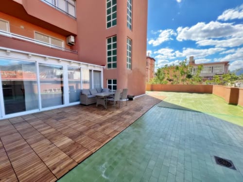 Amplia terraza de apartamento en Fuengirola con tarima de madera, asientos, vistas a la ciudad y jardín bien mantenido