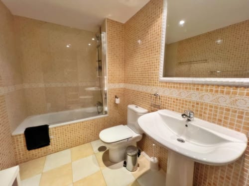 Baño moderno con azulejos mosaico naranja, lavamanos blanco, inodoro y bañera en apartamento de Fuengirola
