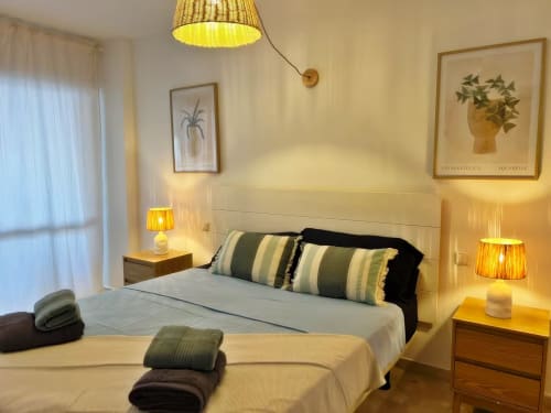 Dormitorio moderno y luminoso en apartamento de Fuengirola con vistas a la ciudad, camas gemelas, almohadas rayadas, iluminación cálida