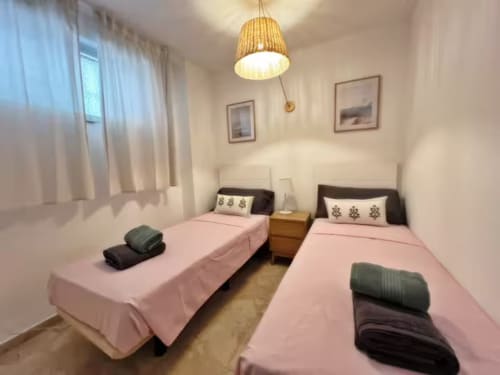 Dormitorio doble en apartamento de Fuengirola con camas rosa, lámpara colgante de madera y vistas a la ciudad