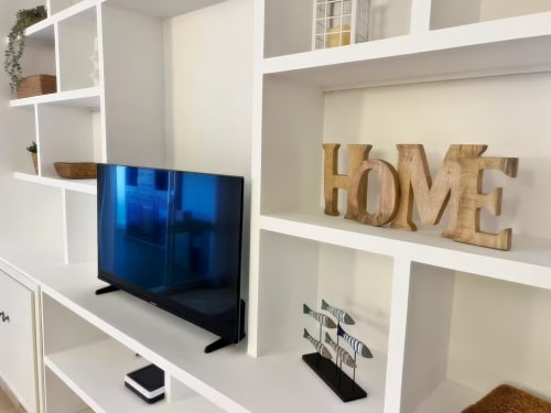 Moderno salón en Fuengirola con estanterías blancas, TV de pantalla plana y decoración de madera HOME