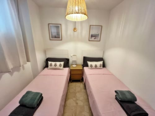 Dormitorio doble en apartamento de Fuengirola con ropa de cama rosa, lámpara colgante de mimbre y vistas a la ciudad