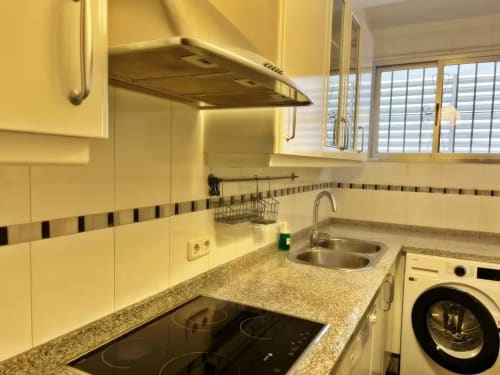 Cocina moderna en apartamento de Fuengirola con armarios color crema, encimera de granito, placa de inducción y lavadora