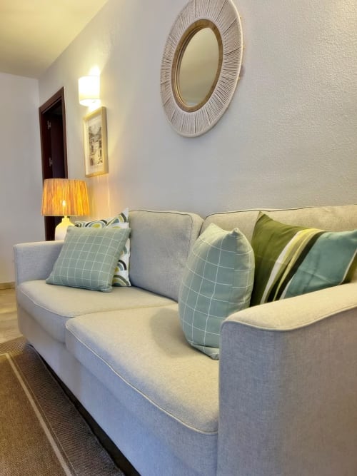 Espacioso salón de apartamento en Fuengirola con sofá beige, cojines decorativos, espejo elegante e iluminación cálida