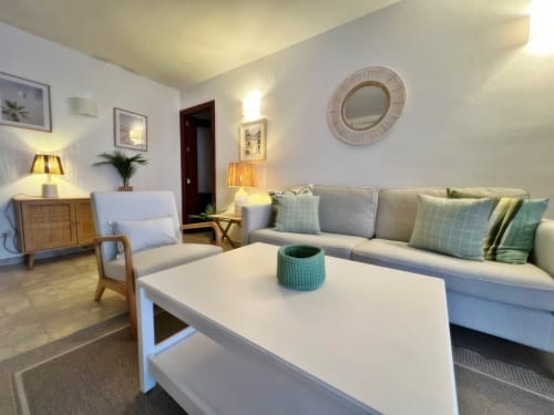Amplio salón de apartamento en Fuengirola con sofá gris, mesa de centro blanca, sillón y vistas a la ciudad