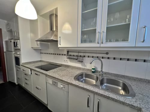 Cocina moderna en apartamento de Fuengirola con muebles blancos, encimeras de granito, fregadero doble de acero inoxidable y campana extractora.