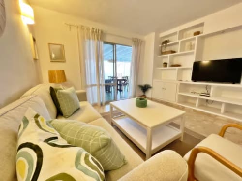 Luminoso apartamento moderno en Fuengirola con sofá crema, estantes blancos, TV y acceso a balcón con vistas al mar