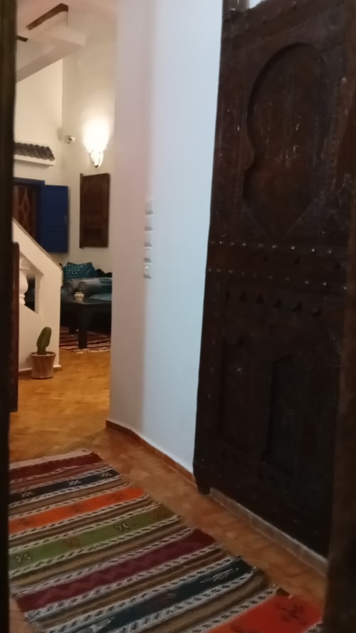 Couloir d'entrée du riad Le Village Mogador à Essaouira avec porte en bois foncé et tapis rayé