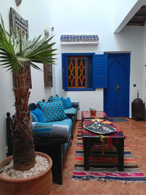 Cour de riad marocain avec portes bleues, canapé turquoise, tapis rayés colorés, palmier et décoration traditionnelle