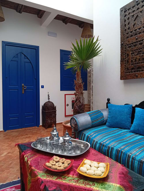 Chambre de riad marocain avec portes bleues, canapé rayé, palmier et service à thé en laiton à Essaouira