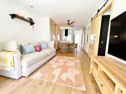 Moderno apartamento de playa en Fuengirola con sofá crema, muebles de madera y alfombra geométrica en salón abierto