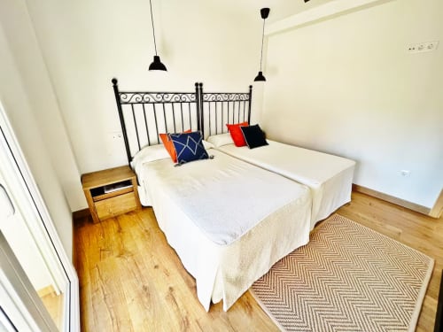 Moderno dormitorio en apartamento de playa Fuengirola con camas gemelas, cabecero de hierro, lámparas colgantes, pisos de madera y diseño contemporáneo