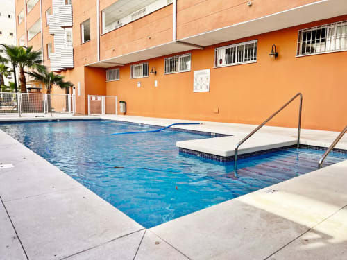 Piscina con vistas al mar en apartamento de playa en Fuengirola, con edificio naranja, tumbonas y palmeras