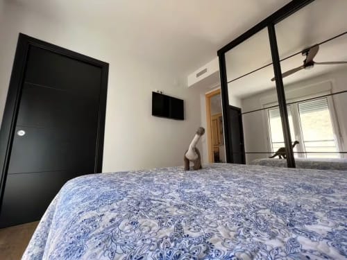 Dormitorio moderno en apartamento Grupo Inmo House Fuengirola con ropa de cama azul estampada, dosel y vista a la ciudad