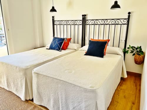 Dos camas gemelas con almohadas decorativas en un apartamento de playa en Fuengirola, con cabeceros de hierro negro y ropa de cama crema