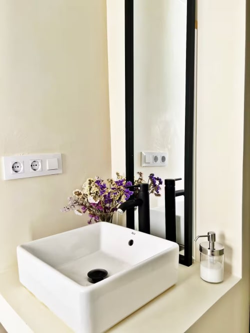 Lavabo moderno con grifo negro, flores púrpuras y espejo en apartamento de playa de Fuengirola