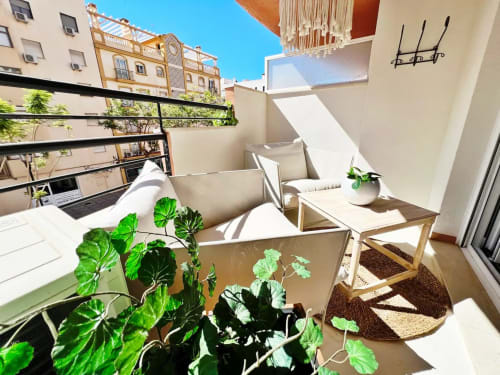 Balcón moderno del apartamento en la playa de Fuengirola con asientos blancos, plantas, vistas a la ciudad y terraza soleada