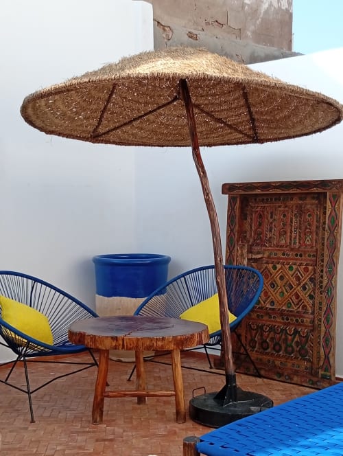 Espace de détente du patio du Riad Le Village Mogador avec parasol tressé, chaises bleues et décor marocain traditionnel à Essaouira