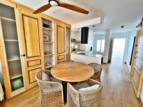 Comedor de apartamento moderno en playa con mesa redonda de madera, sillas tejidas y cocina abierta en Fuengirola