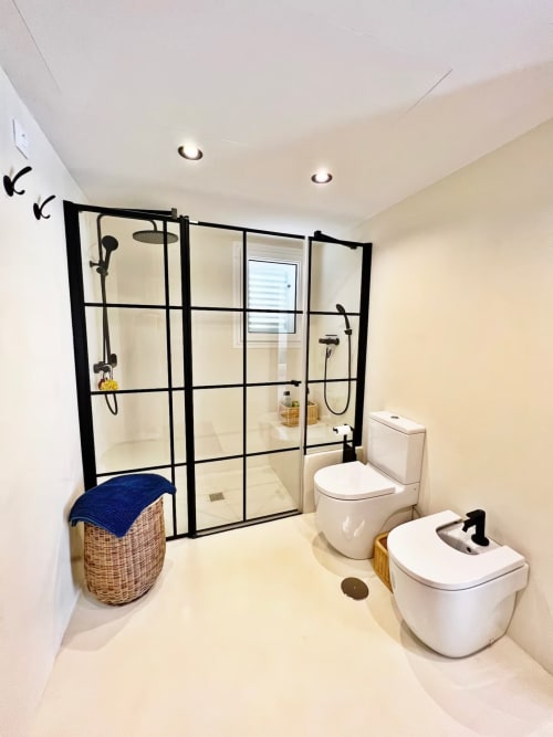Baño moderno en apartamento de playa en Fuengirola con ducha de marco negro, doble lavabo, inodoro y cesto de mimbre