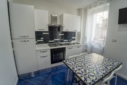 Cucina moderna bianca con rivestimento in piastrelle scure, fornello a gas e pavimento in piastrelle blu nell'appartamento Tramontana presso l'Antico Palazzo del