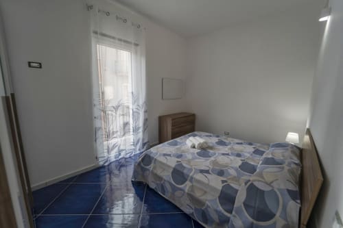 Camera luminosa nell'appartamento Tramontana di Antico Palazzo del Corso con letto a motivi blu, testata in legno e finestra