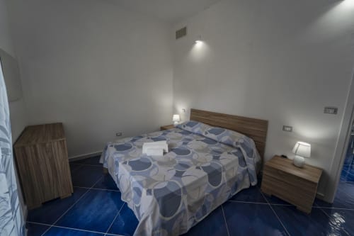 Camera moderna all'Antico Palazzo del Corso con pavimento in piastrelle blu, letto con testata in legno e lampade da comodino a Mirto Crosia