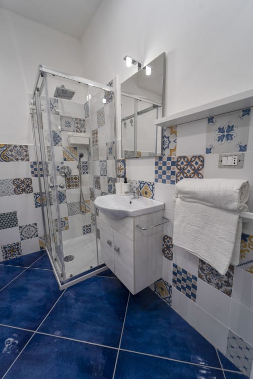 Bagno moderno con pavimento in piastrelle blu, decorative mattonelle portoghesi, vanity bianca, box doccia e porta asciugamani