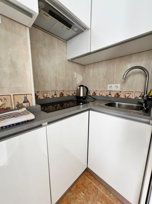 Cocina moderna en apartamento frente al mar, Fuengirola. Gabinetes blancos, encimeras grises, azulejos decorativos y acero inoxidable